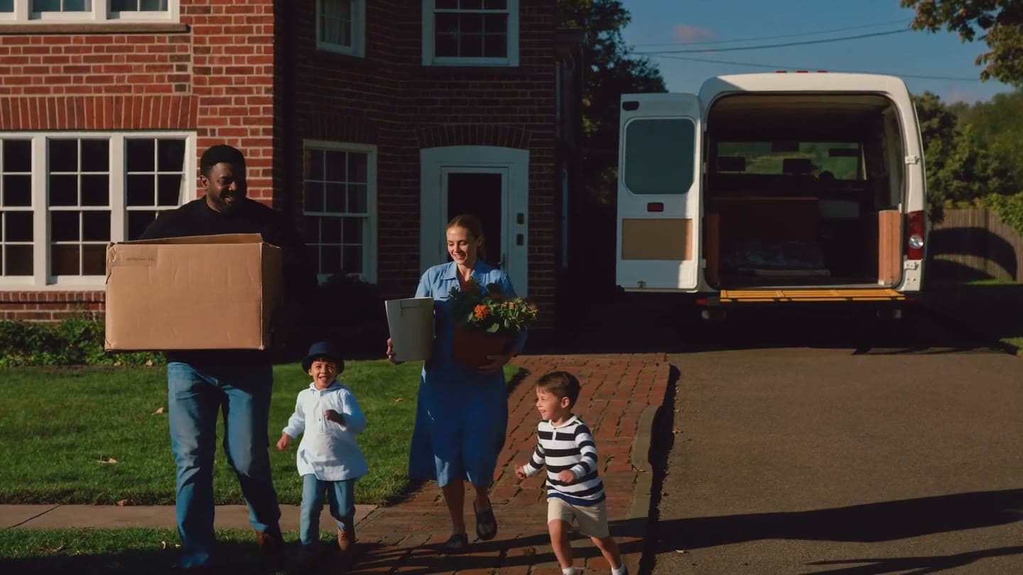A family carry boxes and a plant from the van to their new front door